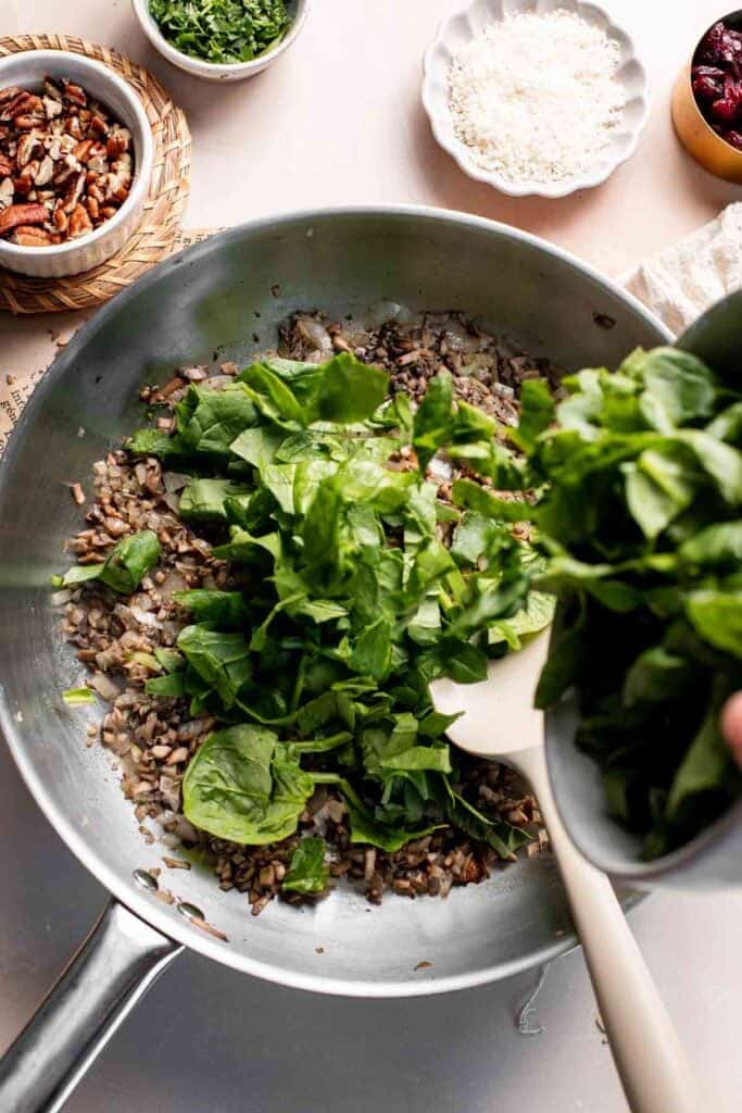 Adding fresh baby spinach to the skillet of mushrooms.