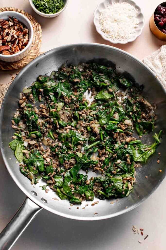 Spinach wilting into the mushroom mixture in the skillet.
