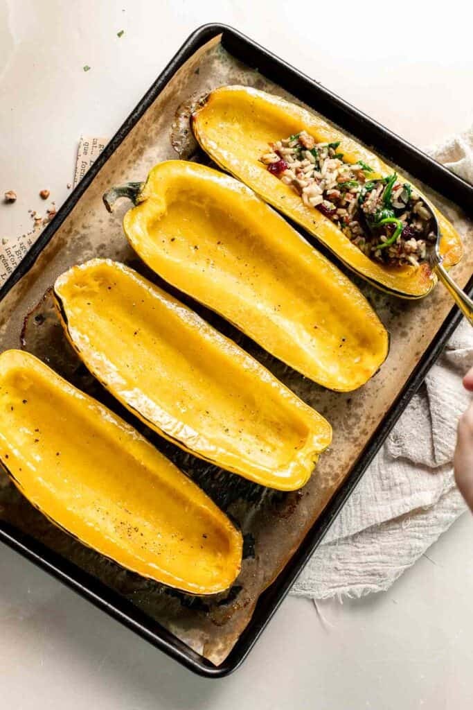 Spooning the wild rice filling into a roasted delicata squash half.