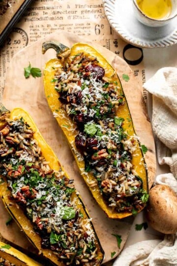 Baked stuffed delicata squash with wild rice, cranberries, pecans, and Parmesan, garnished with fresh parsley on a wooden board.