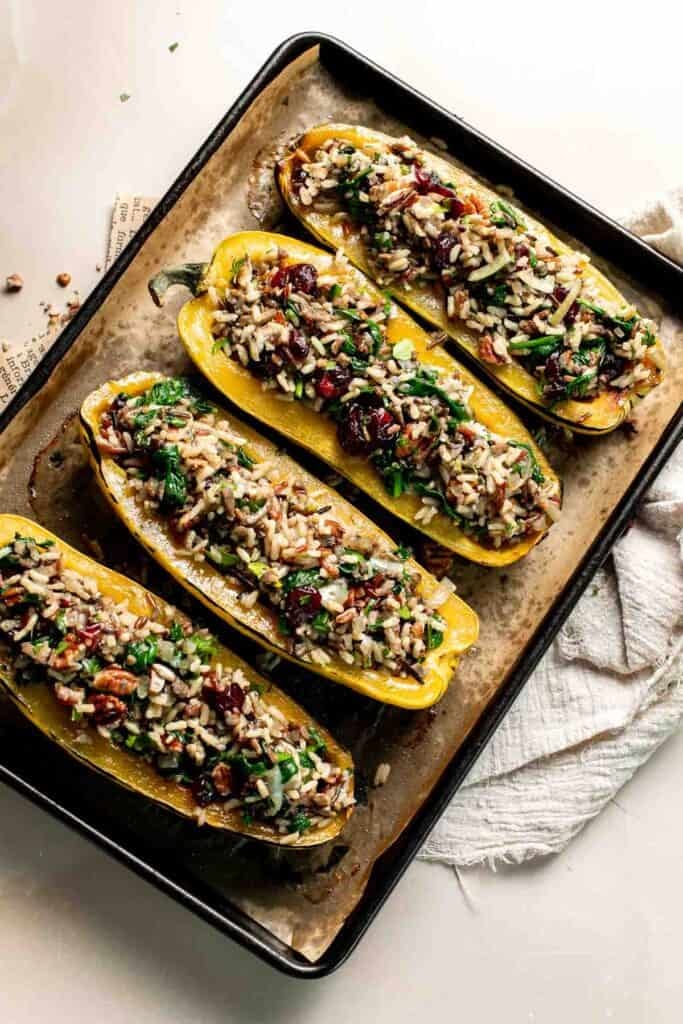 Delicata squash halves filled with wild rice stuffing on a baking sheet.