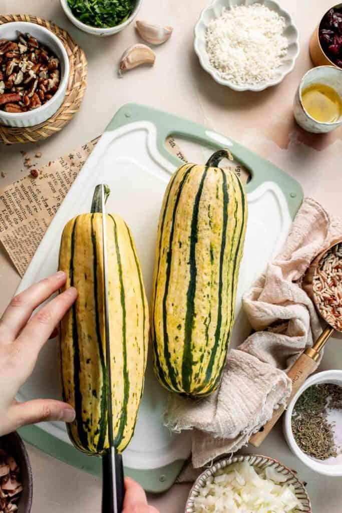 Slicing a delicata squash in half lengthwise on a cutting board.