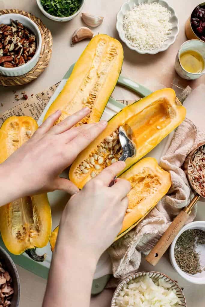 Scooping the seeds out of a delicata squash half with a spoon.