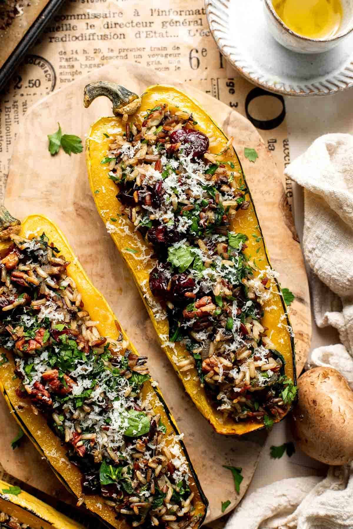 Baked stuffed delicata squash with wild rice, cranberries, pecans, and Parmesan, garnished with fresh parsley on a wooden board.