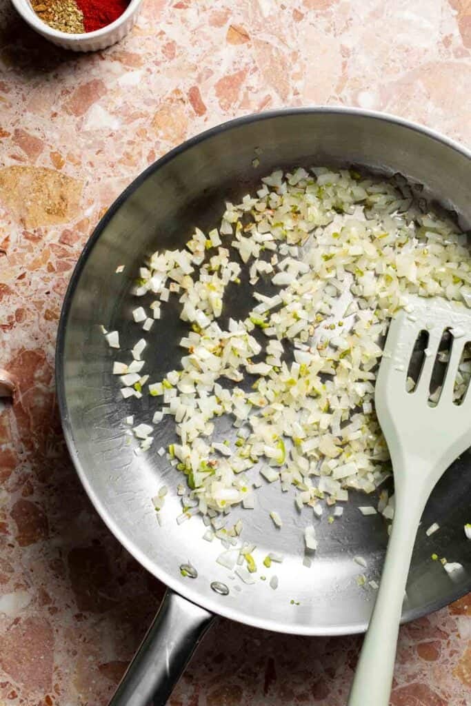 Softened onion and jalapeño cooking in the skillet with a spatula.