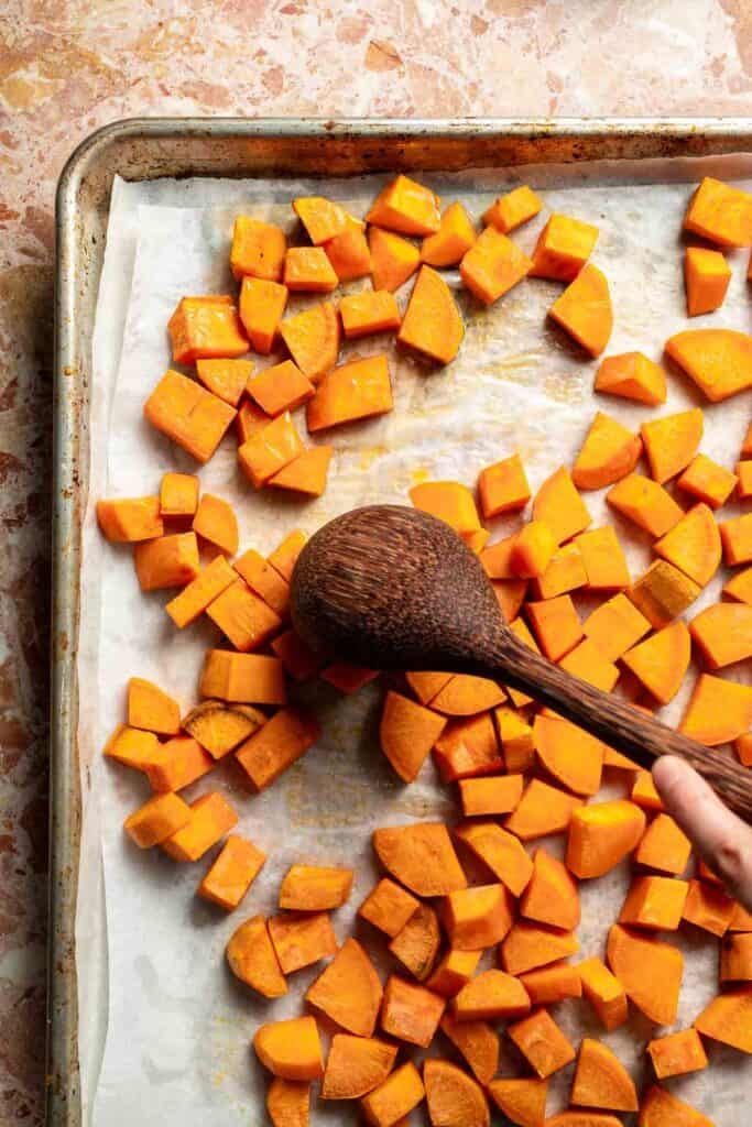 Flipping the roasting sweet potatoes halfway through with a wooden spoon.