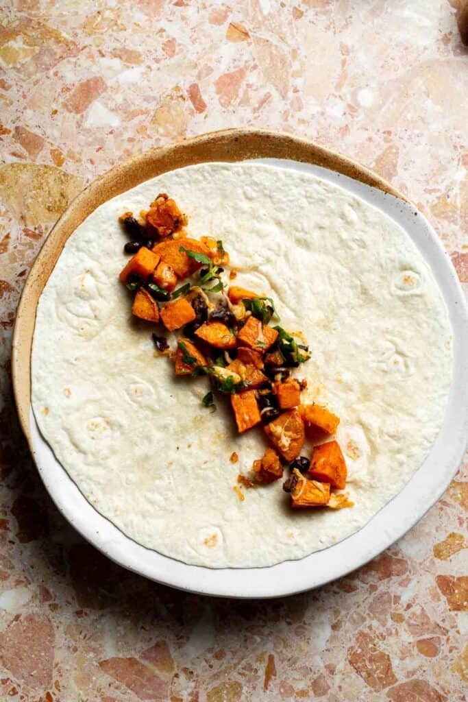 Sweet potato black bean filling spooned down the center of a flour tortilla.