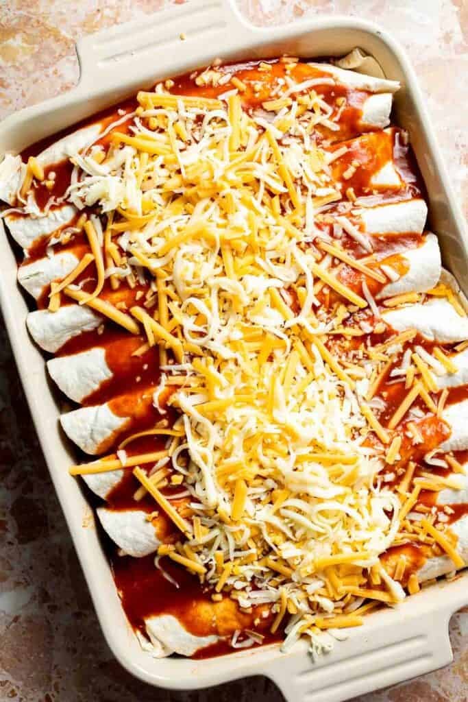 Enchiladas topped with a thick layer of shredded Mexican cheese blend before baking.