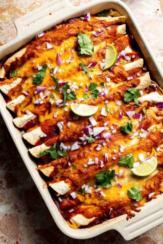 Baked enchiladas garnished with diced red onion, fresh cilantro, and lime wedges.