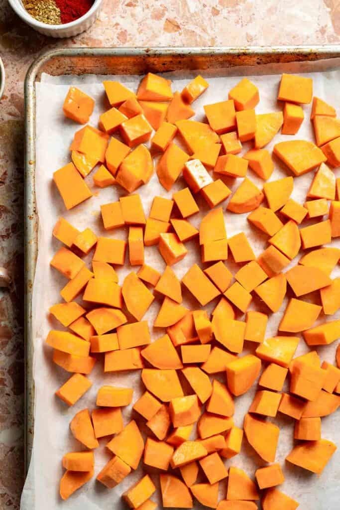 Diced sweet potatoes tossed with olive oil in a single layer on a baking sheet, ready to roast.
