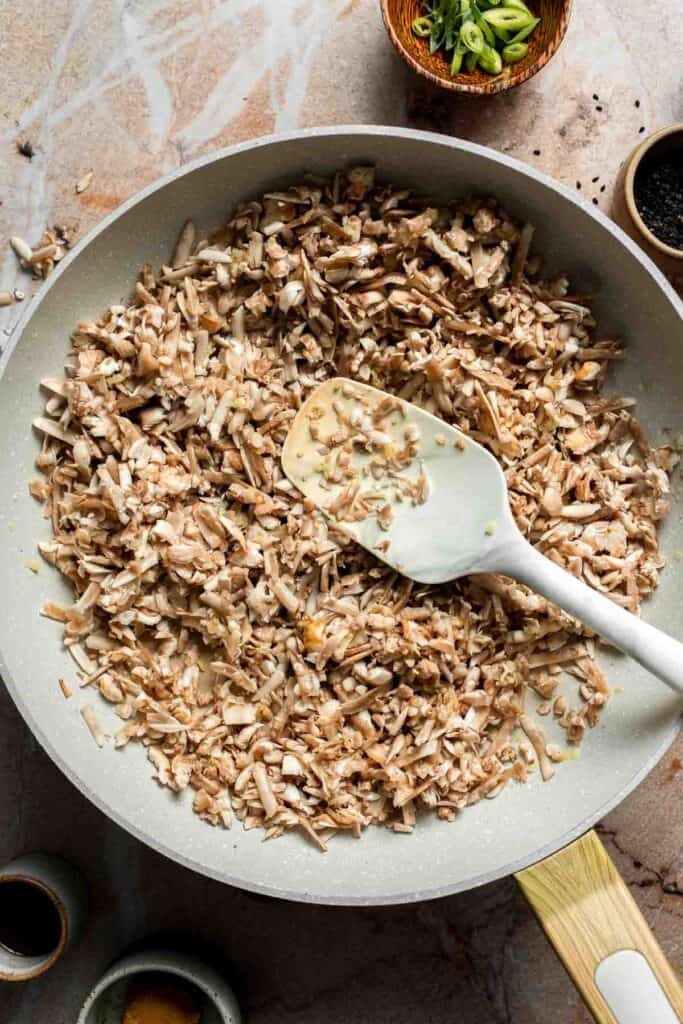 Shredded mushrooms cooking in the skillet with a spatula.