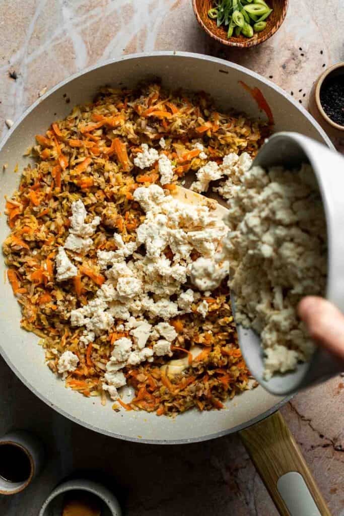 Crumbled tofu being added to the cooked vegetables.