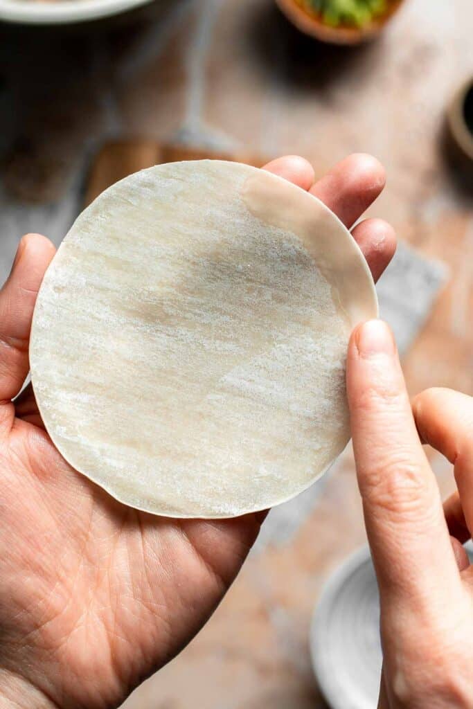Finger moistening the edge of a round dumpling wrapper with water.