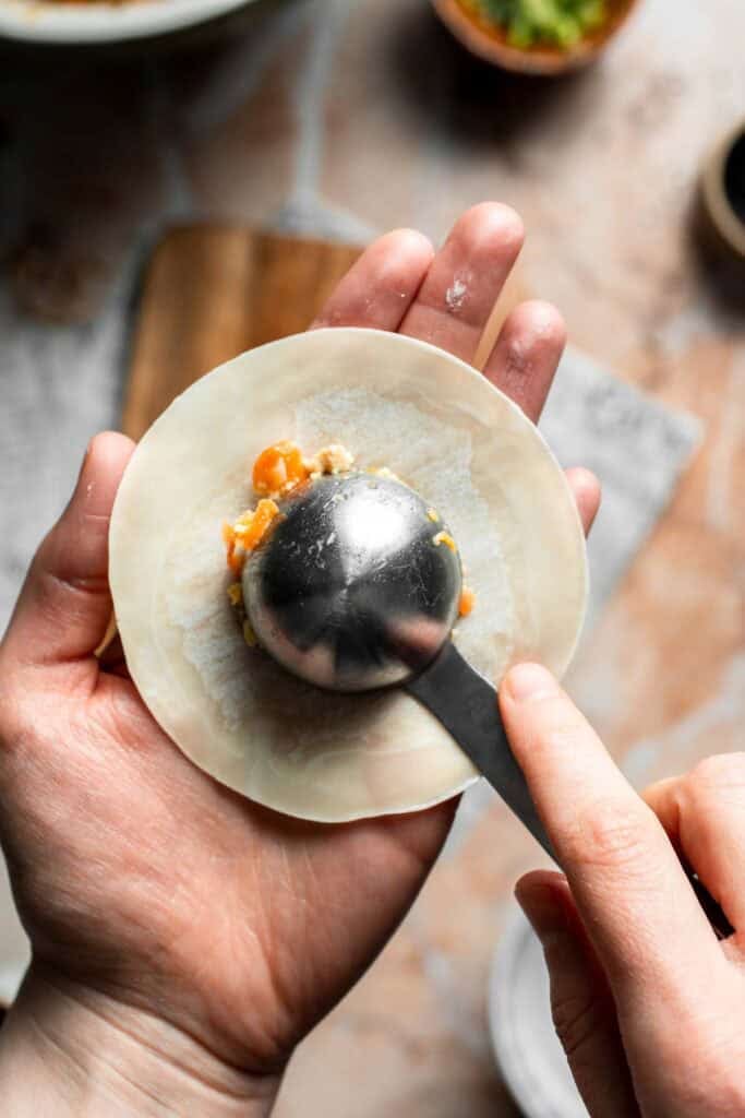 Scooping a spoonful of vegetable filling onto the center of a dumpling wrapper.