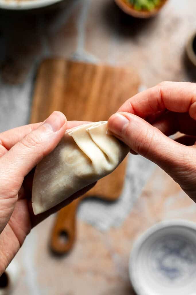 Forming small pleats along the edge of the gyoza.