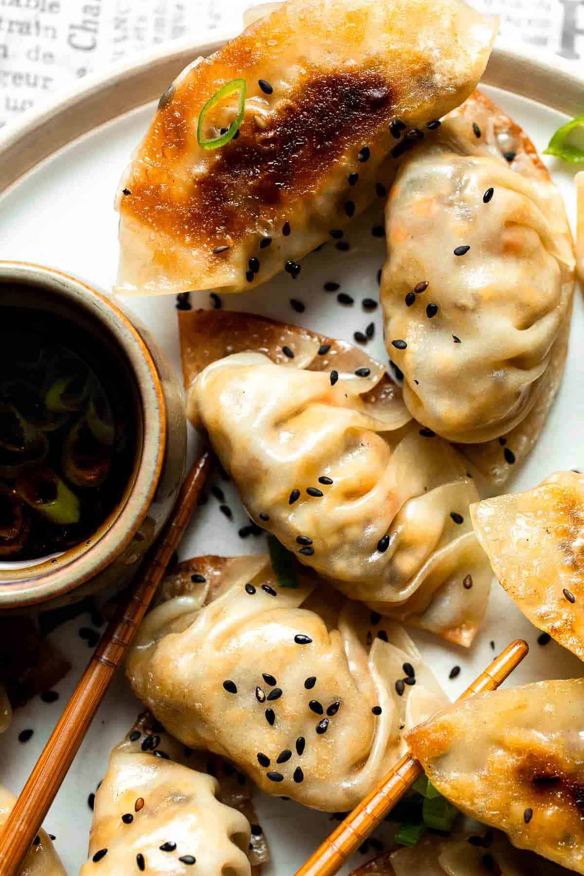 Close-up of golden, crispy vegetable gyoza on a plate with black sesame seeds and dipping sauce.