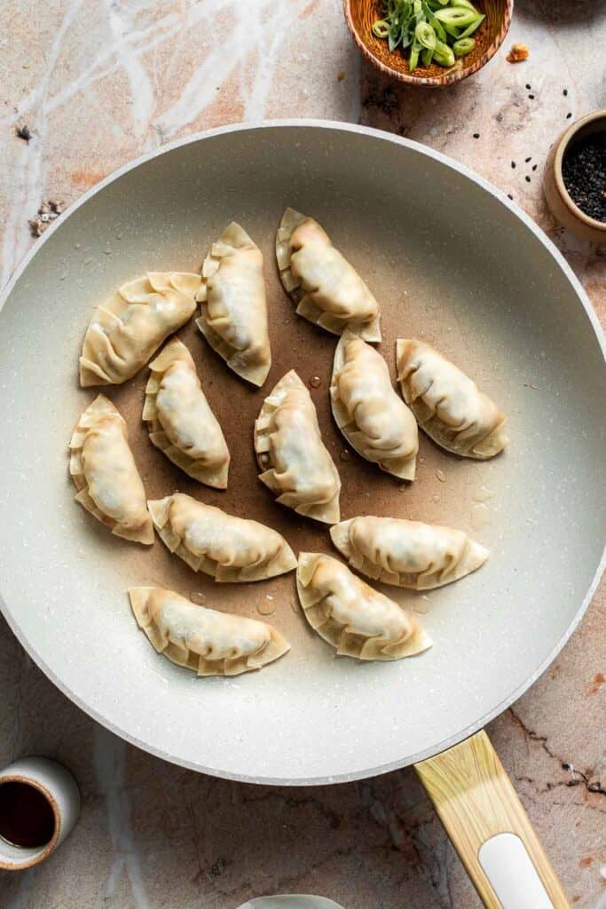 Folded gyoza arranged flat side down in a skillet.