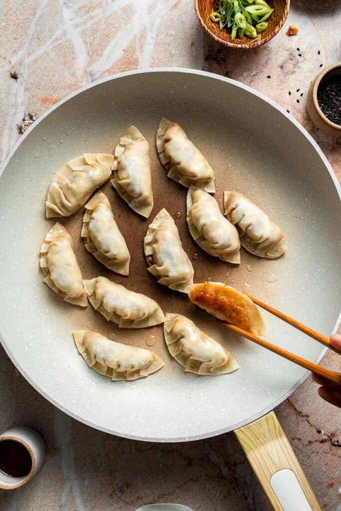 Using chopsticks to check that the bottom of the gyoza is crispy and golden.