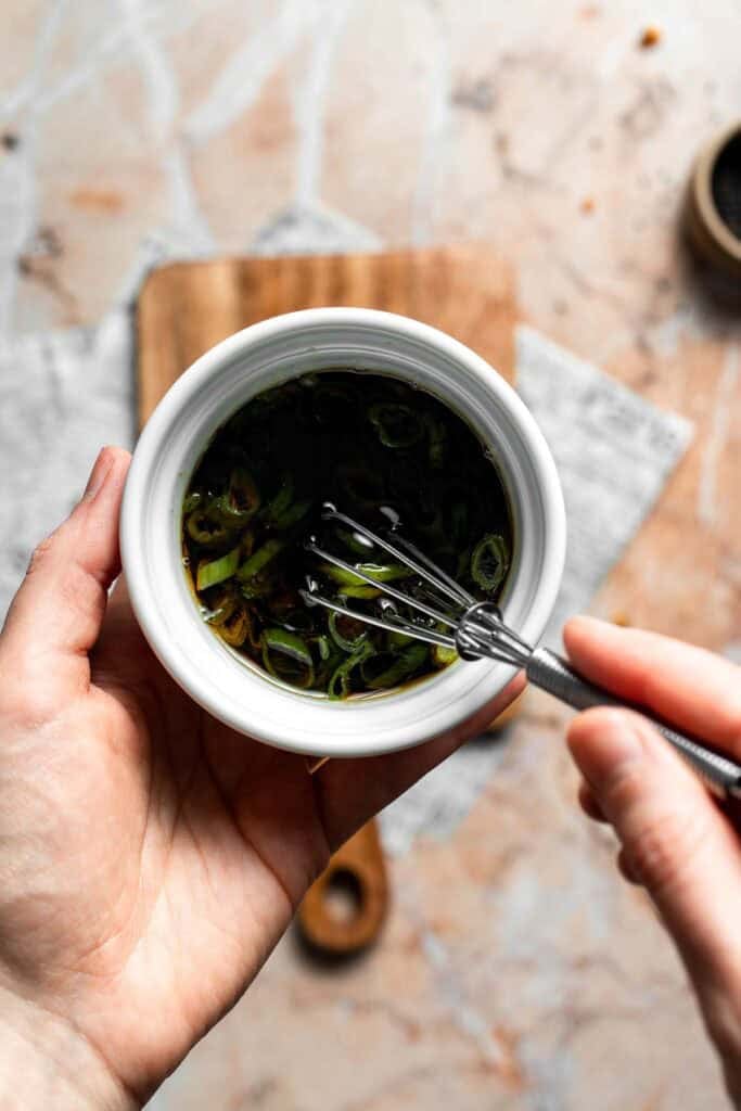 Whisking the dipping sauce with green onions in a small bowl.