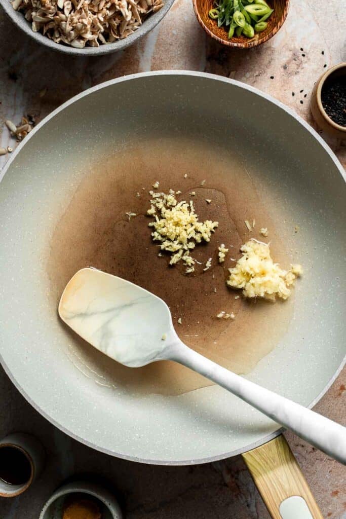 Minced garlic and ginger added to the hot oil in a skillet.