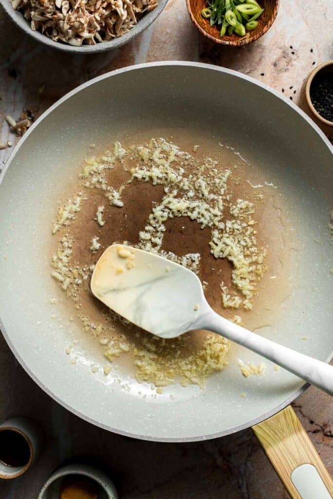 Minced garlic and ginger sizzling in the skillet, stirred with a spatula.