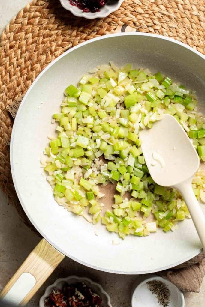 Softened onion and celery cooking in the skillet with a spatula.