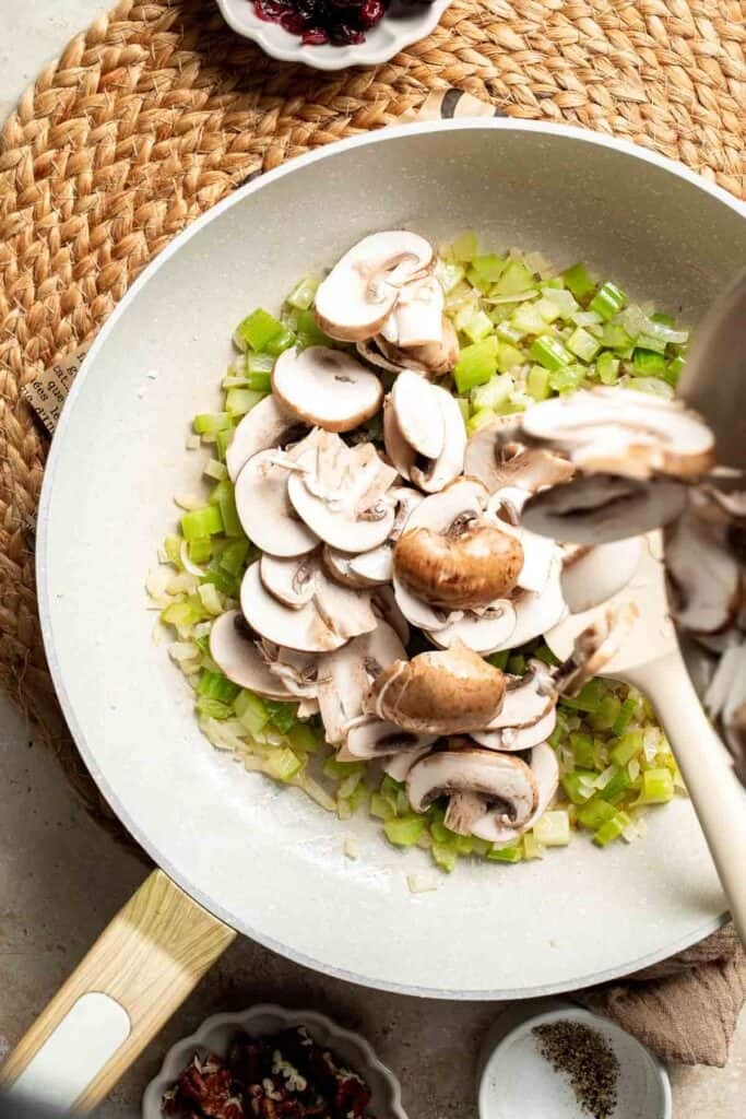 Sliced cremini mushrooms added to the skillet with the onion and celery.