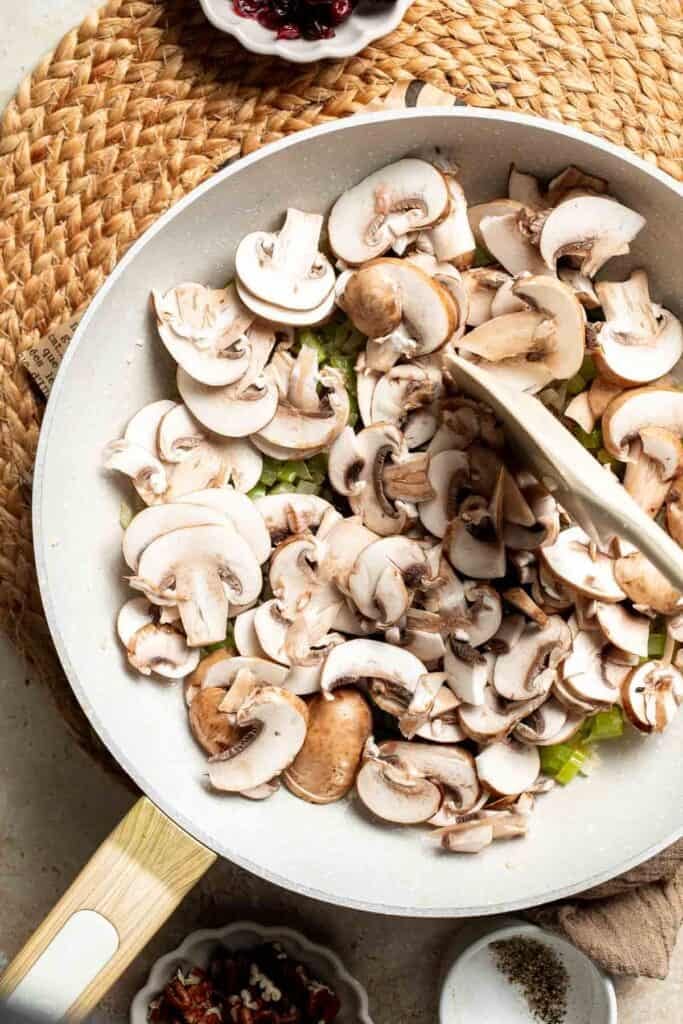 Sliced cremini mushrooms added to the skillet with the onion and celery.