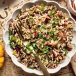 Bowl of wild rice stuffing with mushrooms, dried cranberries, pecans, and parsley, served with a gold spoon.