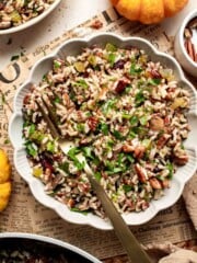 Bowl of wild rice stuffing with mushrooms, dried cranberries, pecans, and parsley, served with a gold spoon.