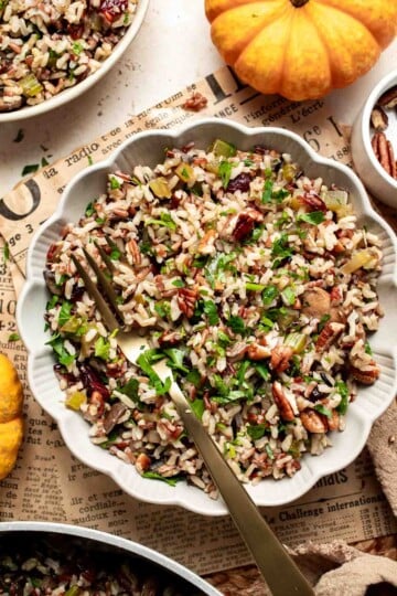 Bowl of wild rice stuffing with mushrooms, dried cranberries, pecans, and parsley, served with a gold spoon.