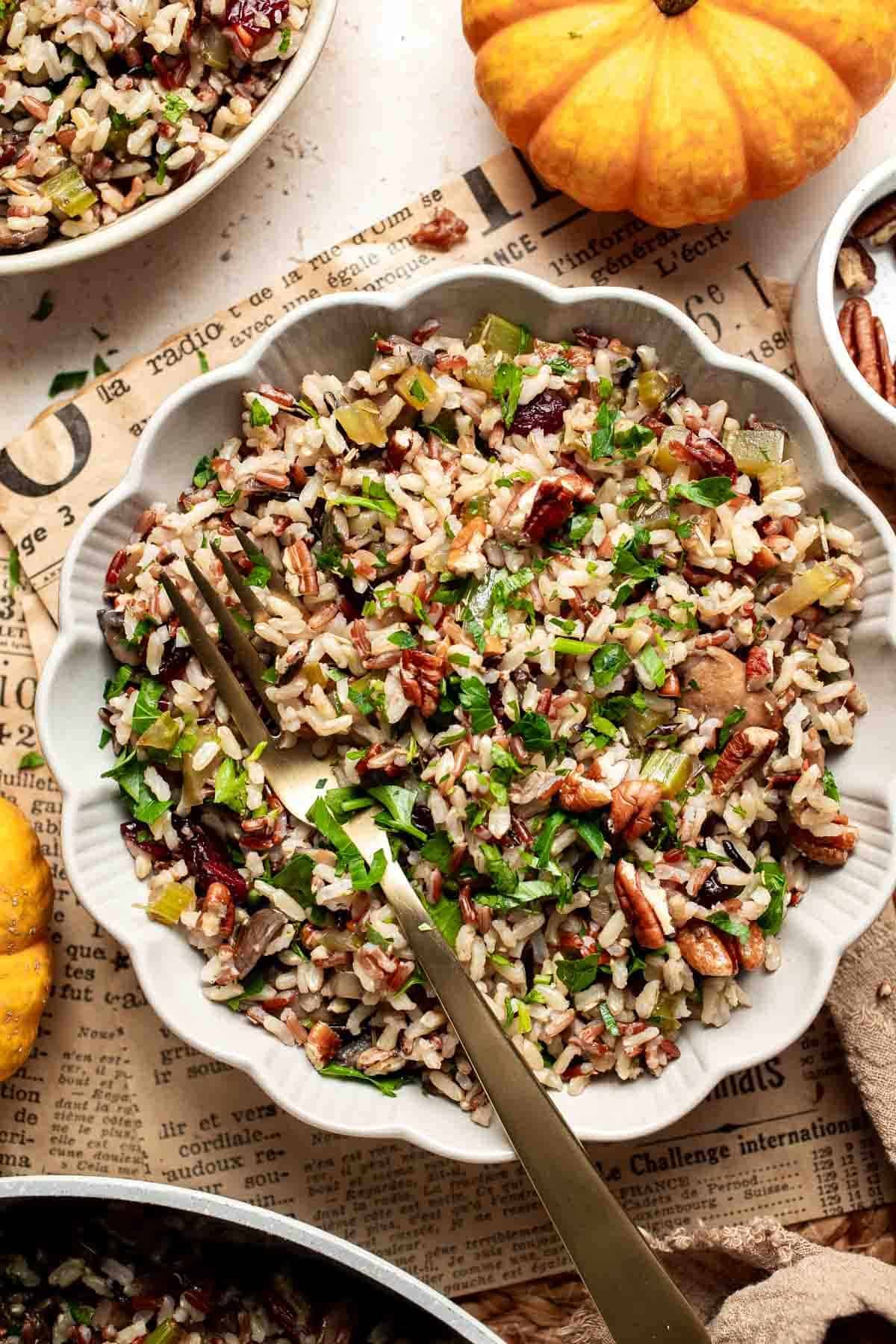 Bowl of wild rice stuffing with mushrooms, dried cranberries, pecans, and parsley, served with a gold spoon.