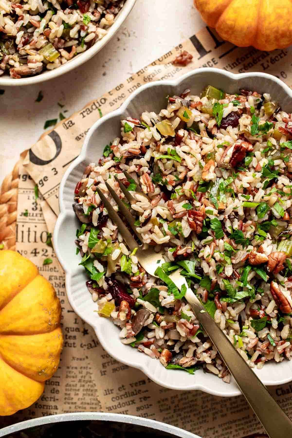 Overhead view of wild rice stuffing in a scalloped bowl with a gold fork and mini pumpkins.