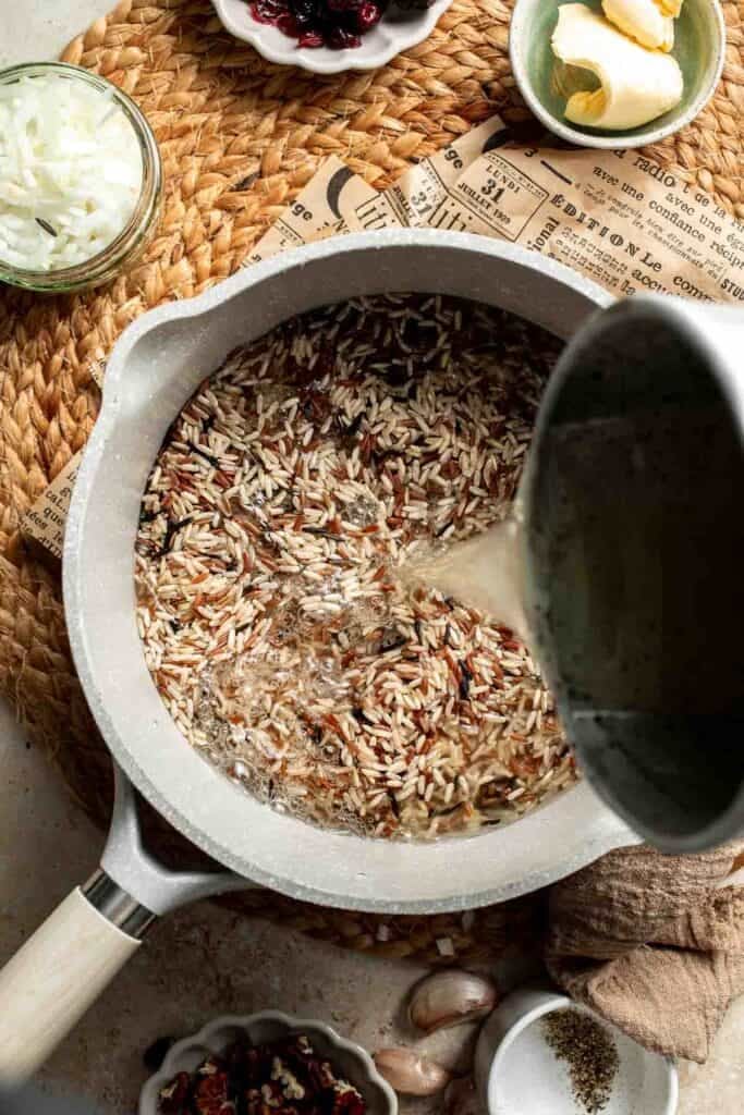 Pouring vegetable broth into the saucepan of wild rice blend.